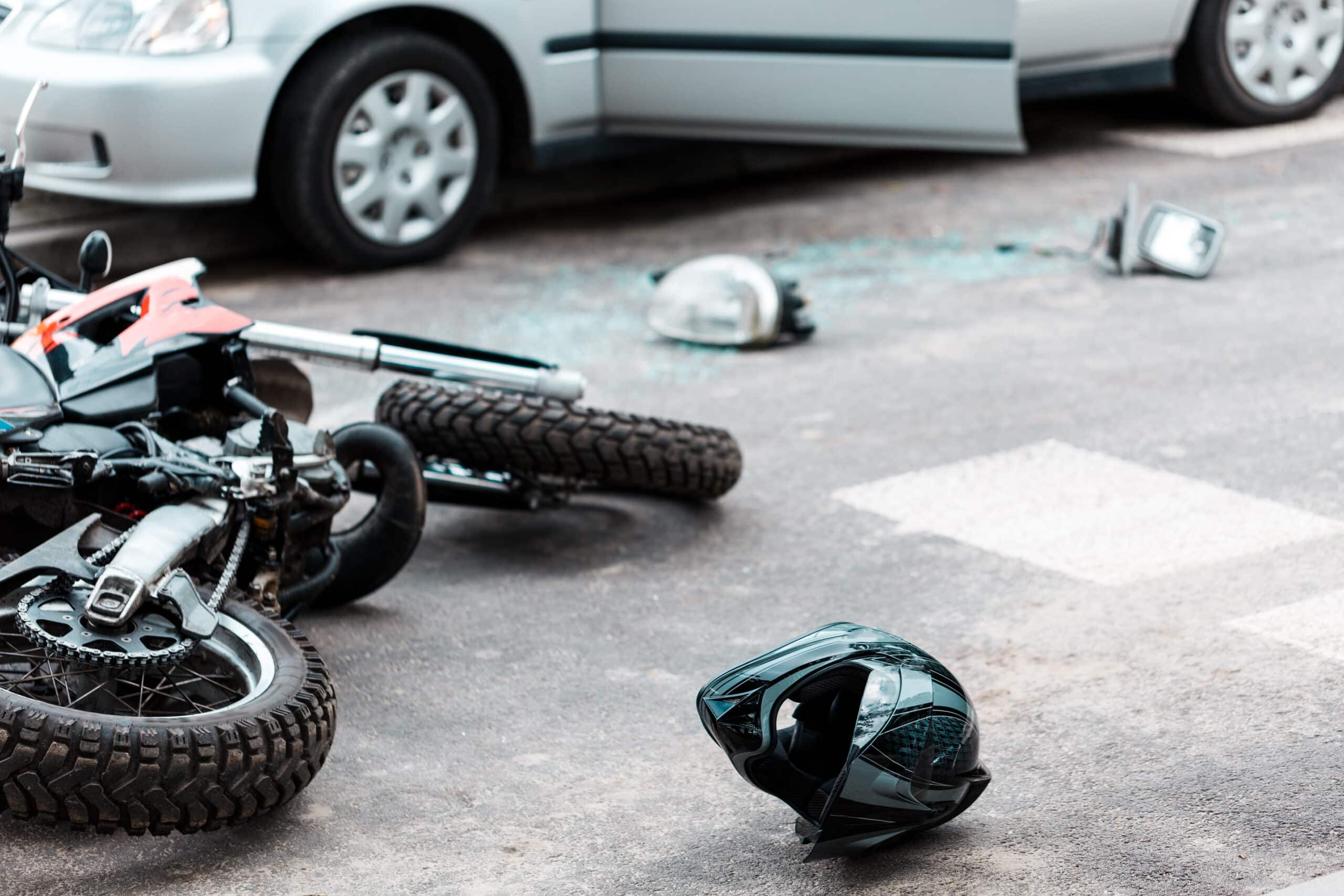 Overturned motorcycle and helmet on the street after a collision with a car, showing accident aftermath in an urban setting.